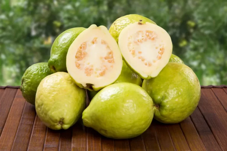 גויאבה חצויה מונחת על ערימת גויאבות טריות על שולחן עץ