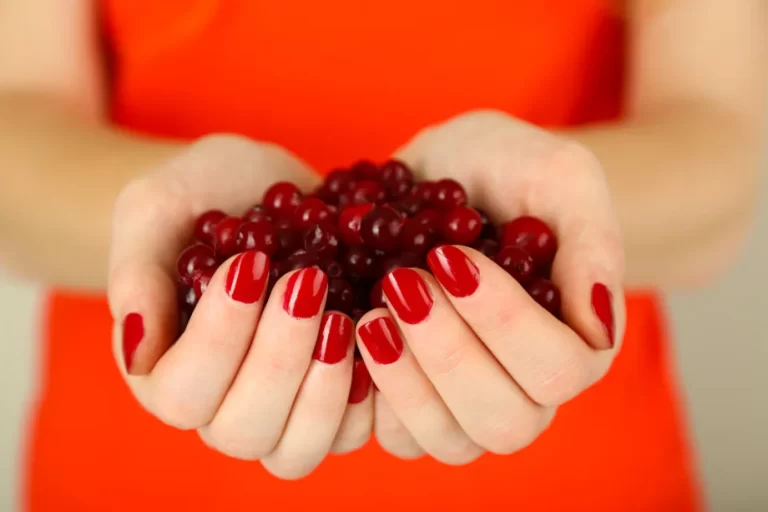 אישה בחולצה אדומה מציגה ציפורניים בריאות ומחזיקה פירות יער קטנים בכפות ידיה