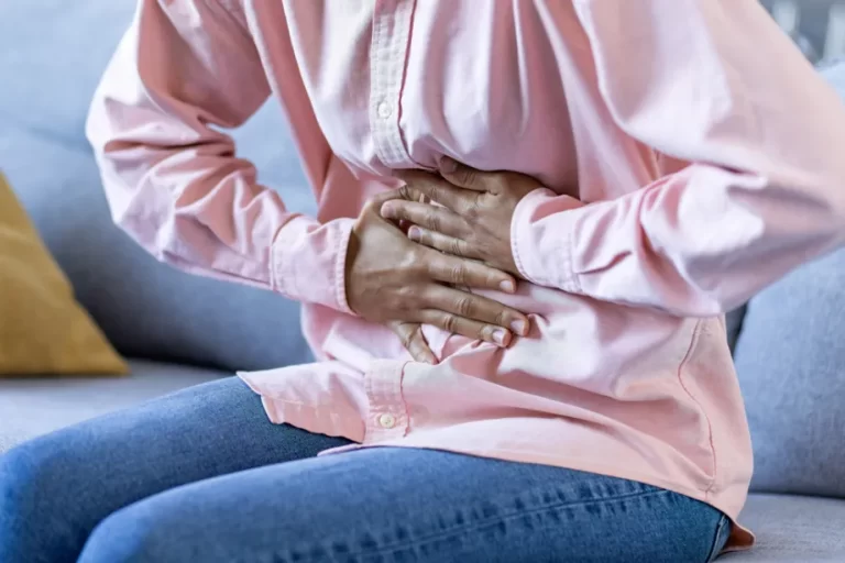 אישה עם תחושת בחילות יושבת ומניחה את כפות ידיה על הבטן